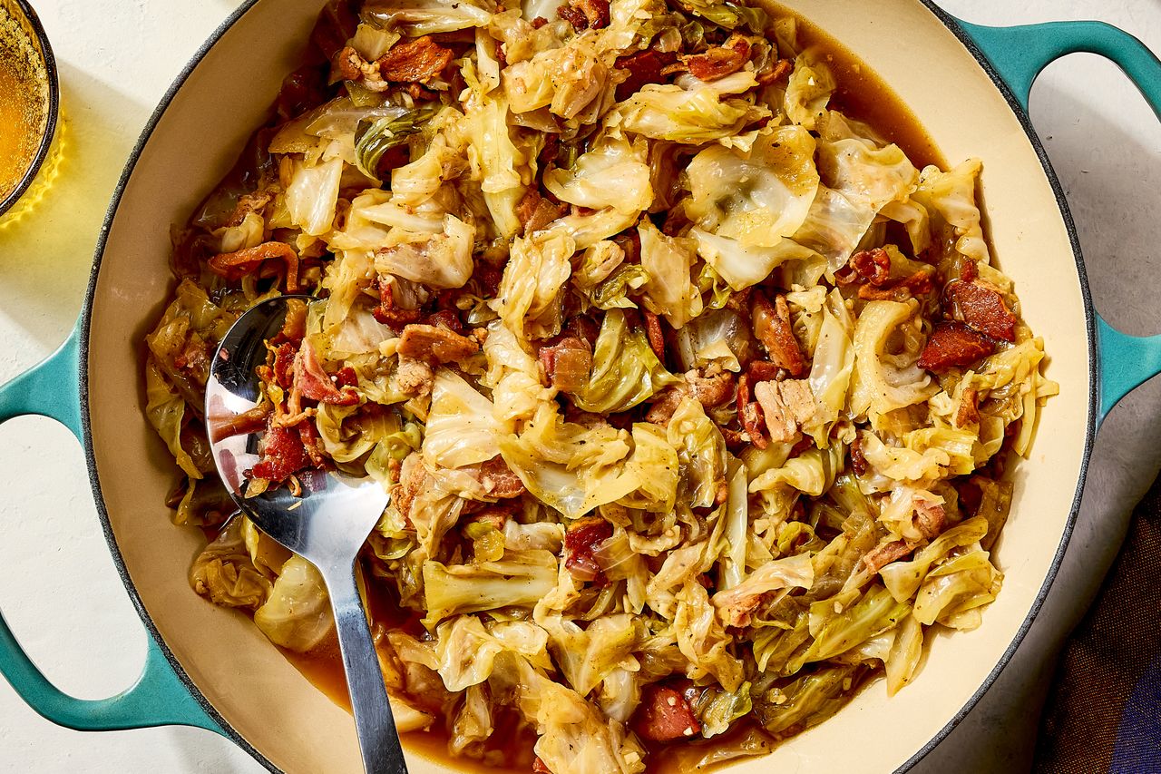 Cooked cabbage with pieces of bacon and other ingredients in a large bluehandled dish with a spoon