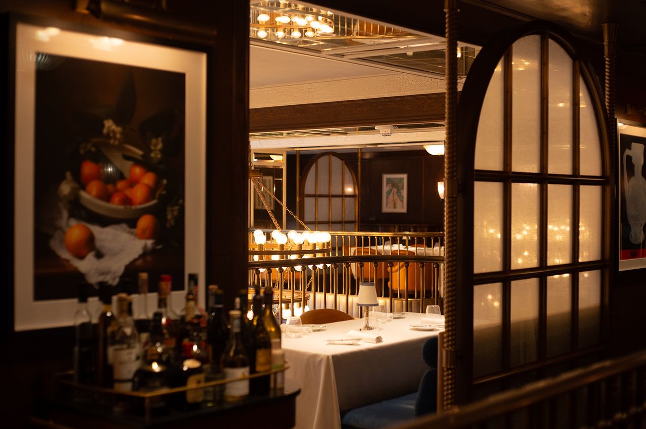 A dining area with tables set for service visible through a window opening with bottles displayed in the foreground