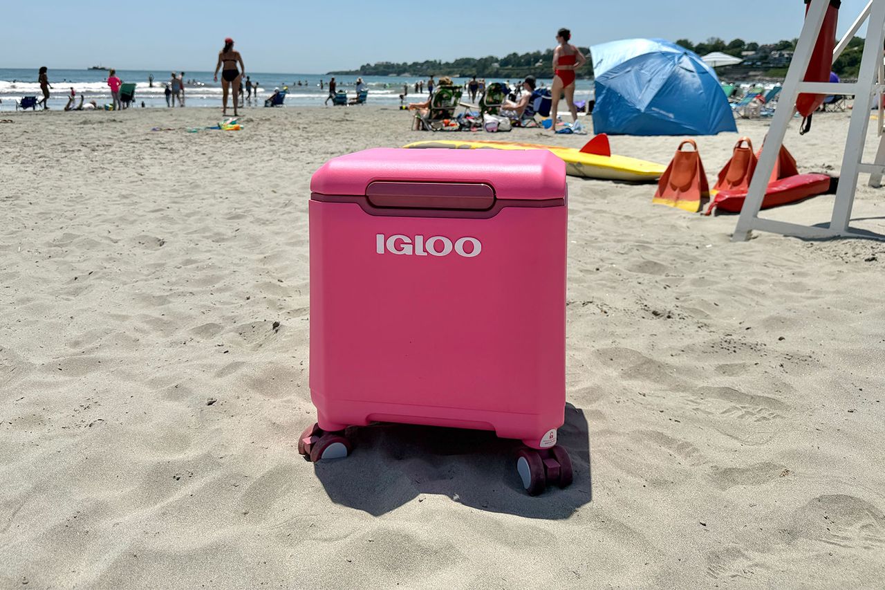 Portable cooler on a sandy beach in front of people and umbrellas