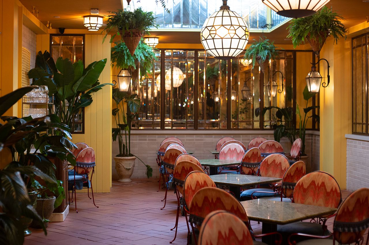 A view of the interior seating area of a restaurant with decorative lighting hanging plants and tables with chairs