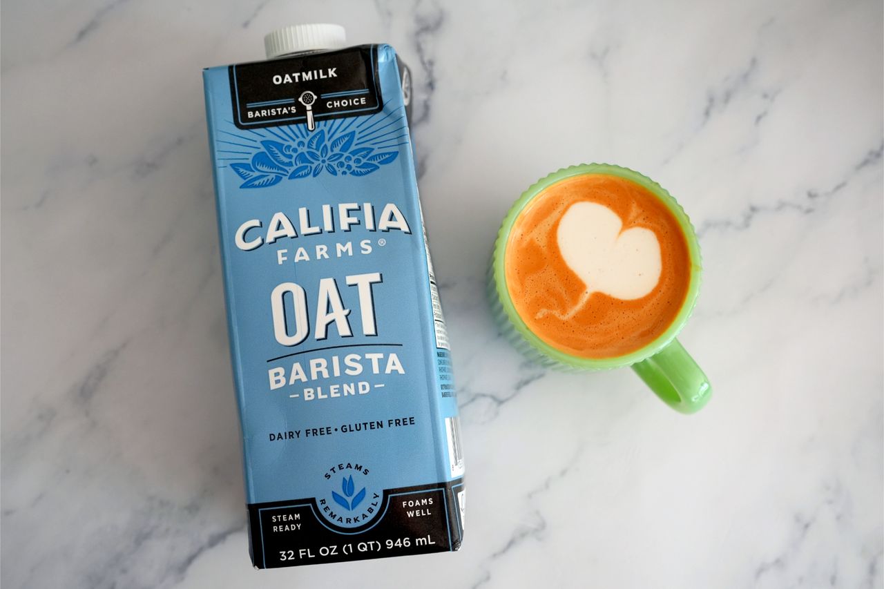 Carton of Califia Farms Oat Barista Blend next to a latte in a green mug with foam art