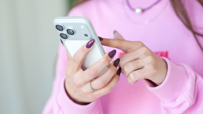 A woman in a pink shirt with painted nails using a white iPhone 17 Pro Max