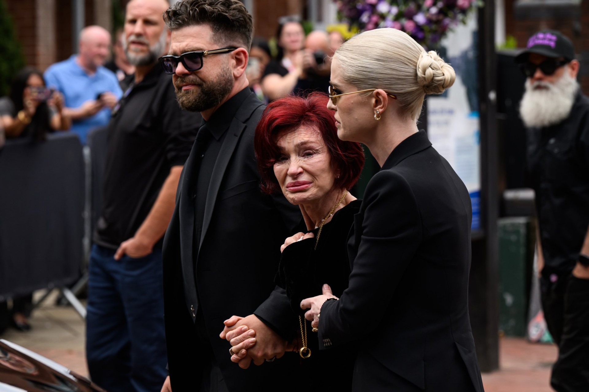 (L-R) Jack Osbourne, Sharon Osbourne and Kelly Osbourne leave after viewing tributes to the late Ozzy Osbourne from fans as his funeral cortege travels through his home city of Birmingham on July 30, 2025