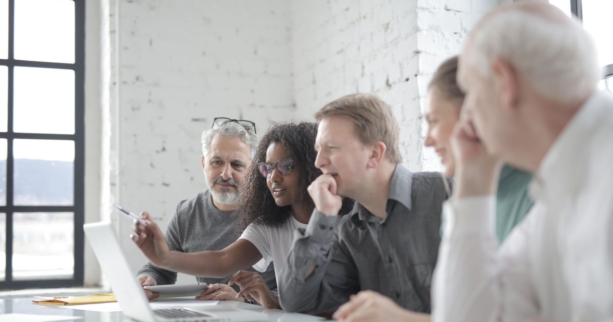Glad multiethnic colleagues watching netbook screen during work process in comfortable office while African American female employee with pen explaining workplace strategy
