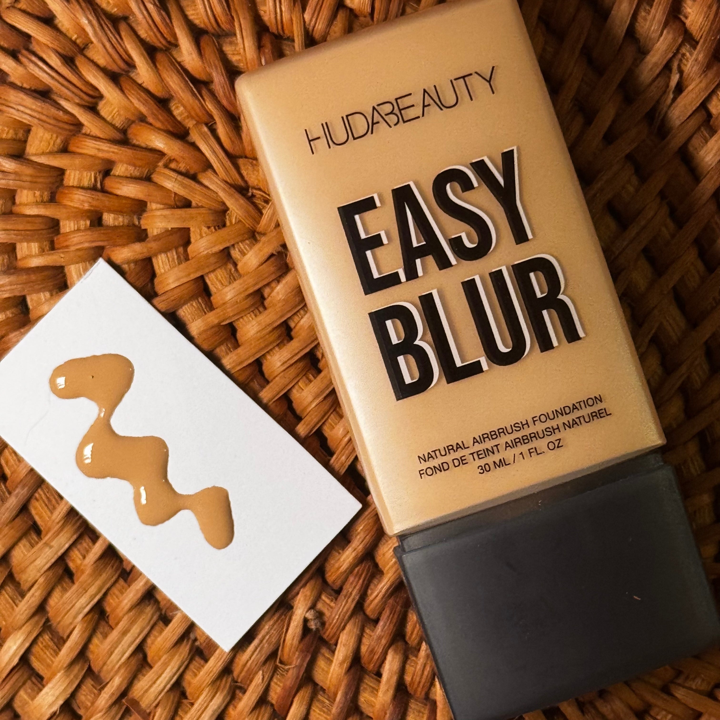 Huda Beauty Easy Blur foundation tube in shade Custard 220N and a swatch on paper placed on a woven surface