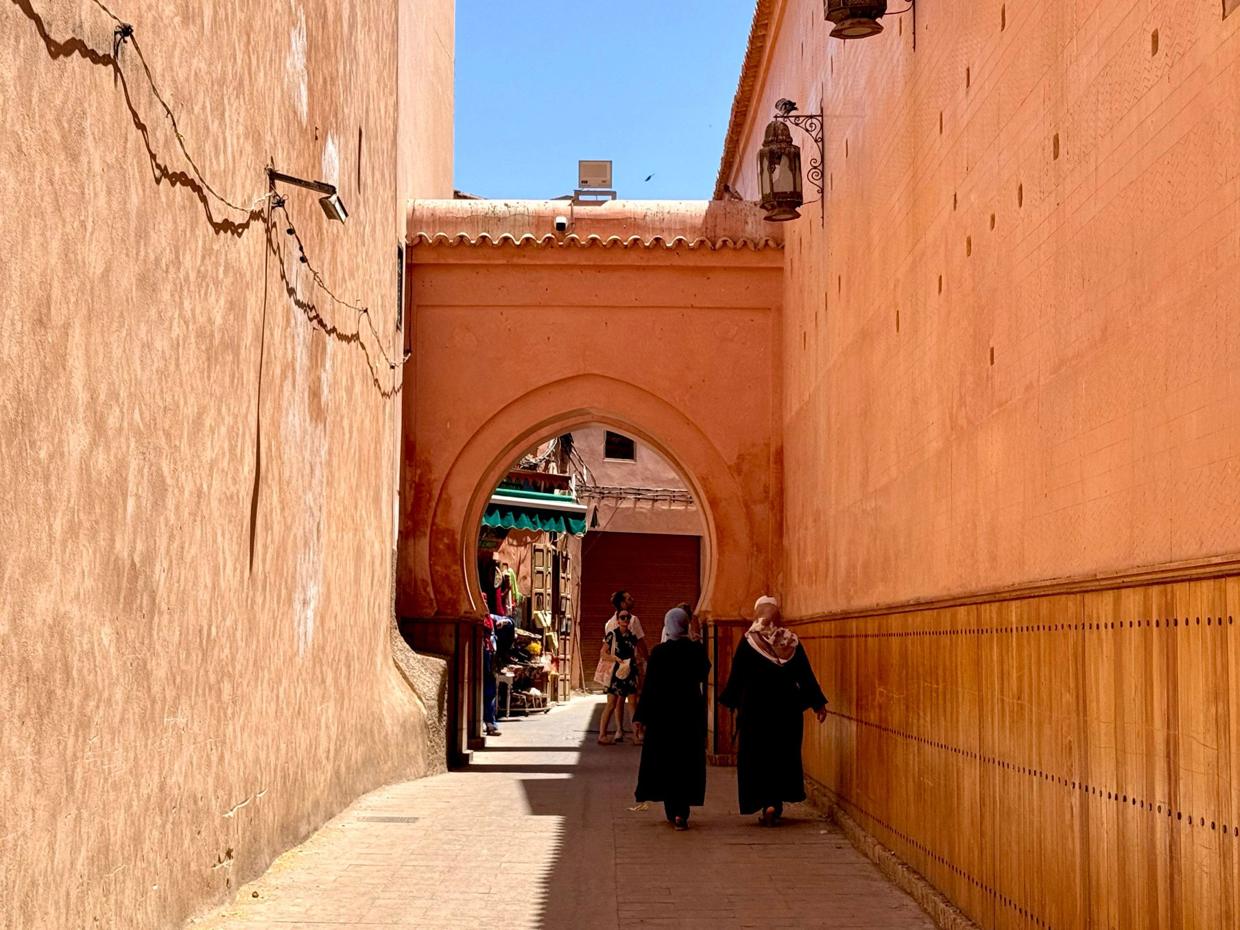 Two women walk towards an arch between two large red buildings in Marrakech