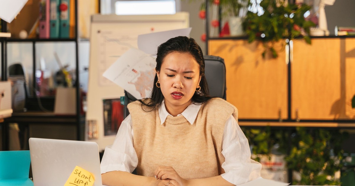 An office worker showing frustration while sitting at a cluttered desk with a laptop.