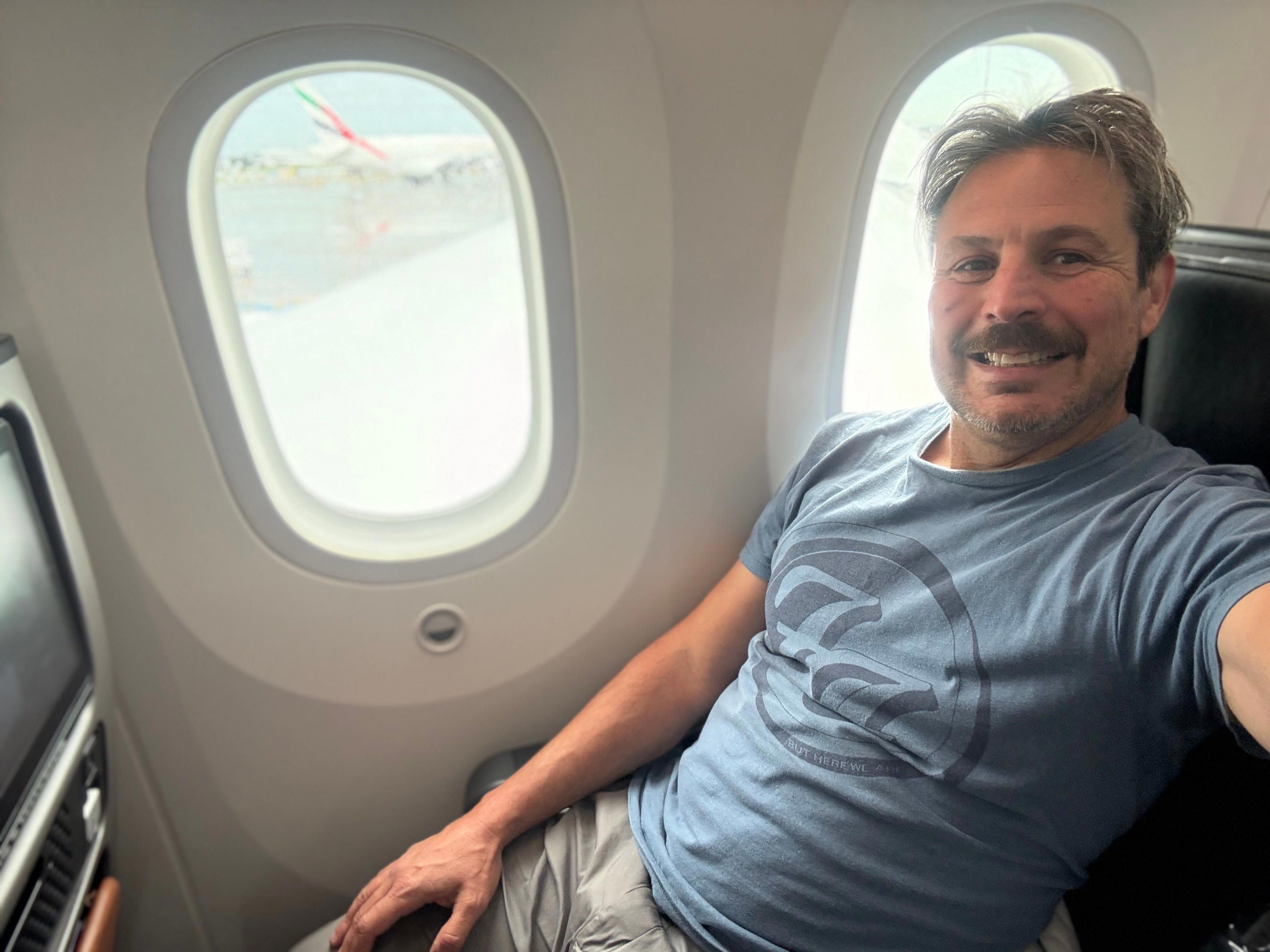 Author Ash Jurberg in premium economy seat next to window, smilnig