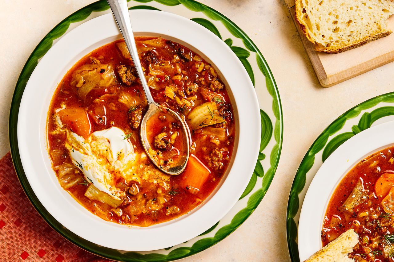 Cabbage roll soup served in a white bowl with a spoon garnished with sour cream surrounded by bread