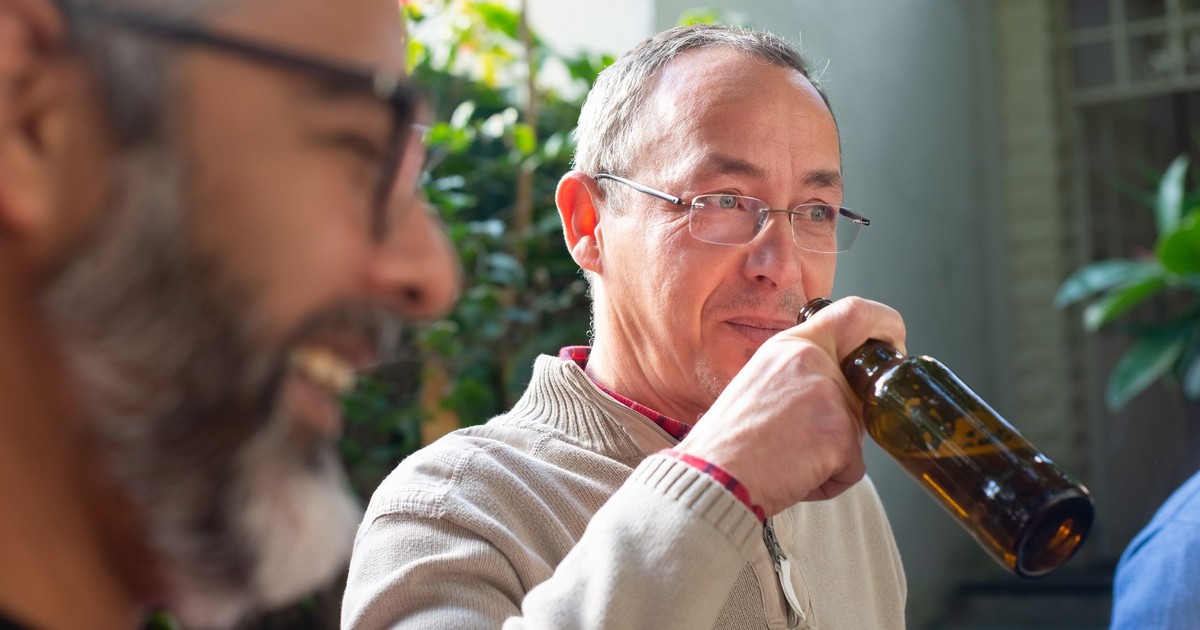 Two senior men enjoying drinks outdoors in a sunny and relaxed setting with greenery.