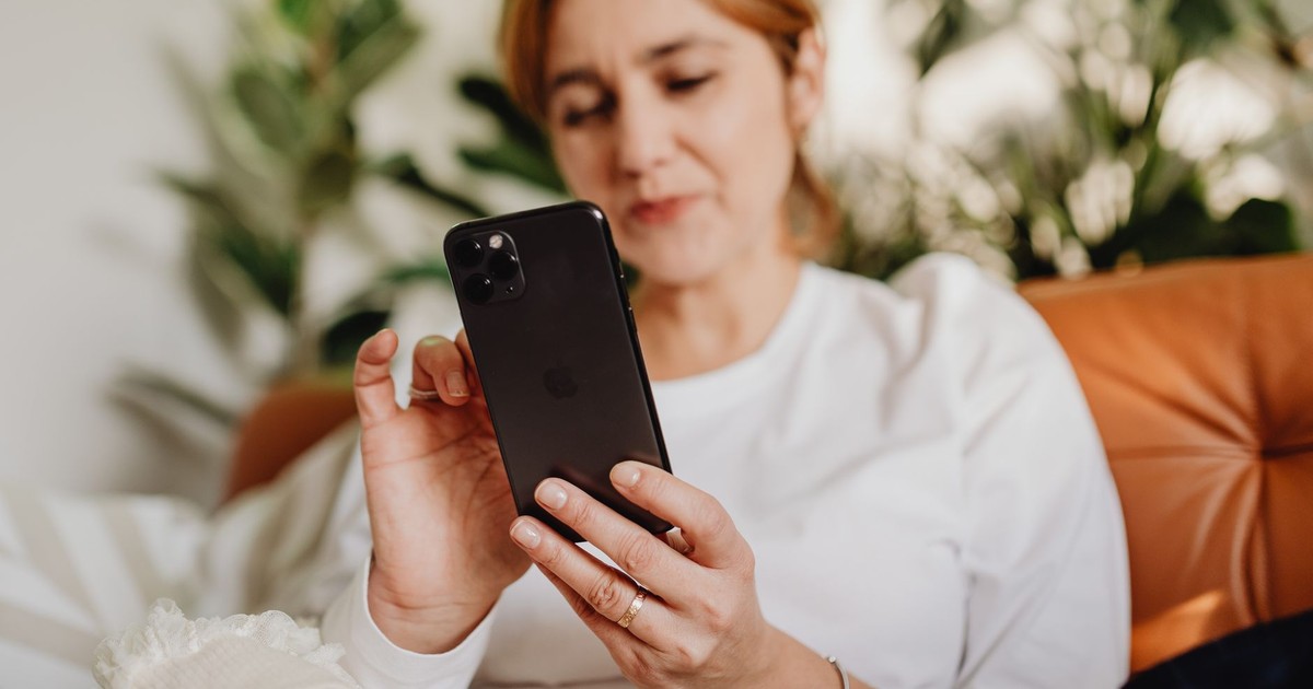 Woman comfortably sitting indoors using a smartphone with plants in the background.