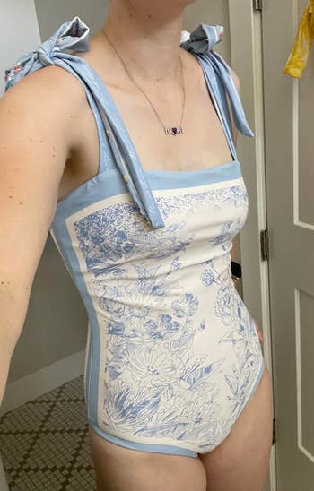 Person wearing a patterned one-piece swimsuit with tied shoulder straps, indoors