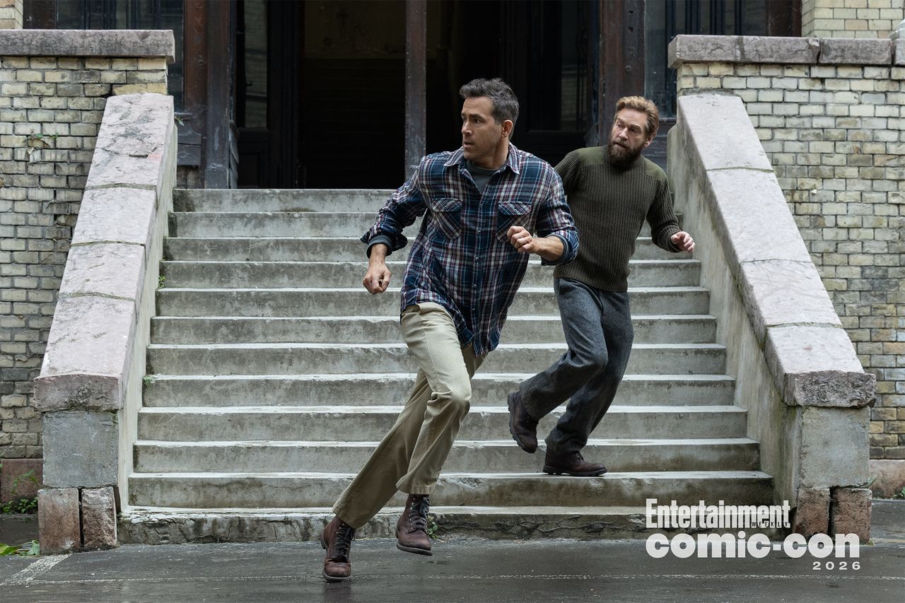 Ryan Reynolds and another person descending outdoor steps in an action pose wearing casual clothes near a brick building