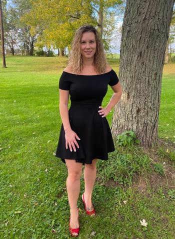 Person in an off-shoulder black dress and red shoes standing in a park setting