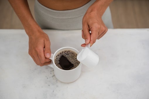 Person adding a sugar cube to a cup of coffee on a white table