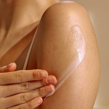 Person applying lotion to their shoulder, focusing on skincare routine for smooth and healthy skin
