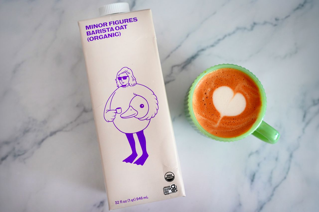 A carton of Minor Figures Barista Oat milk next to a cup filled with latte art
