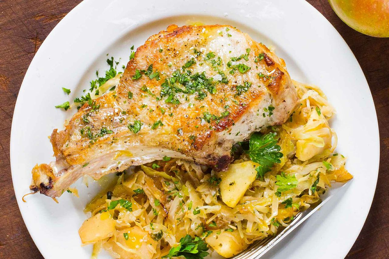 Cooked pork chop served on a bed of cabbage and apple slices on a white plate