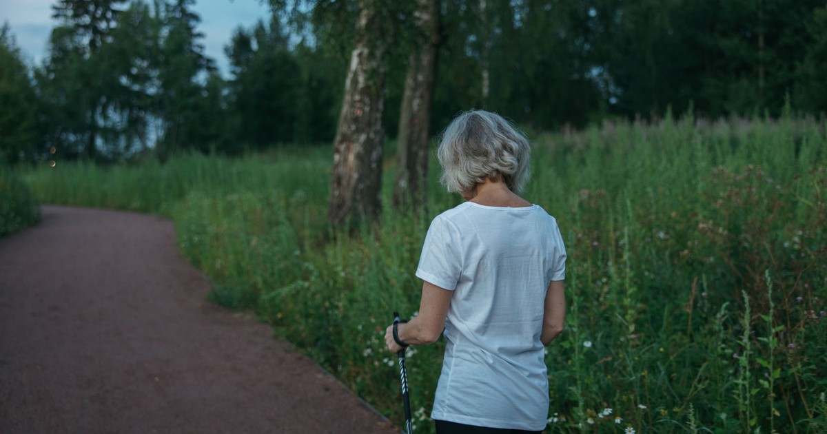 Elderly woman practicing Nordic walking on a park trail, promoting health and fitness.