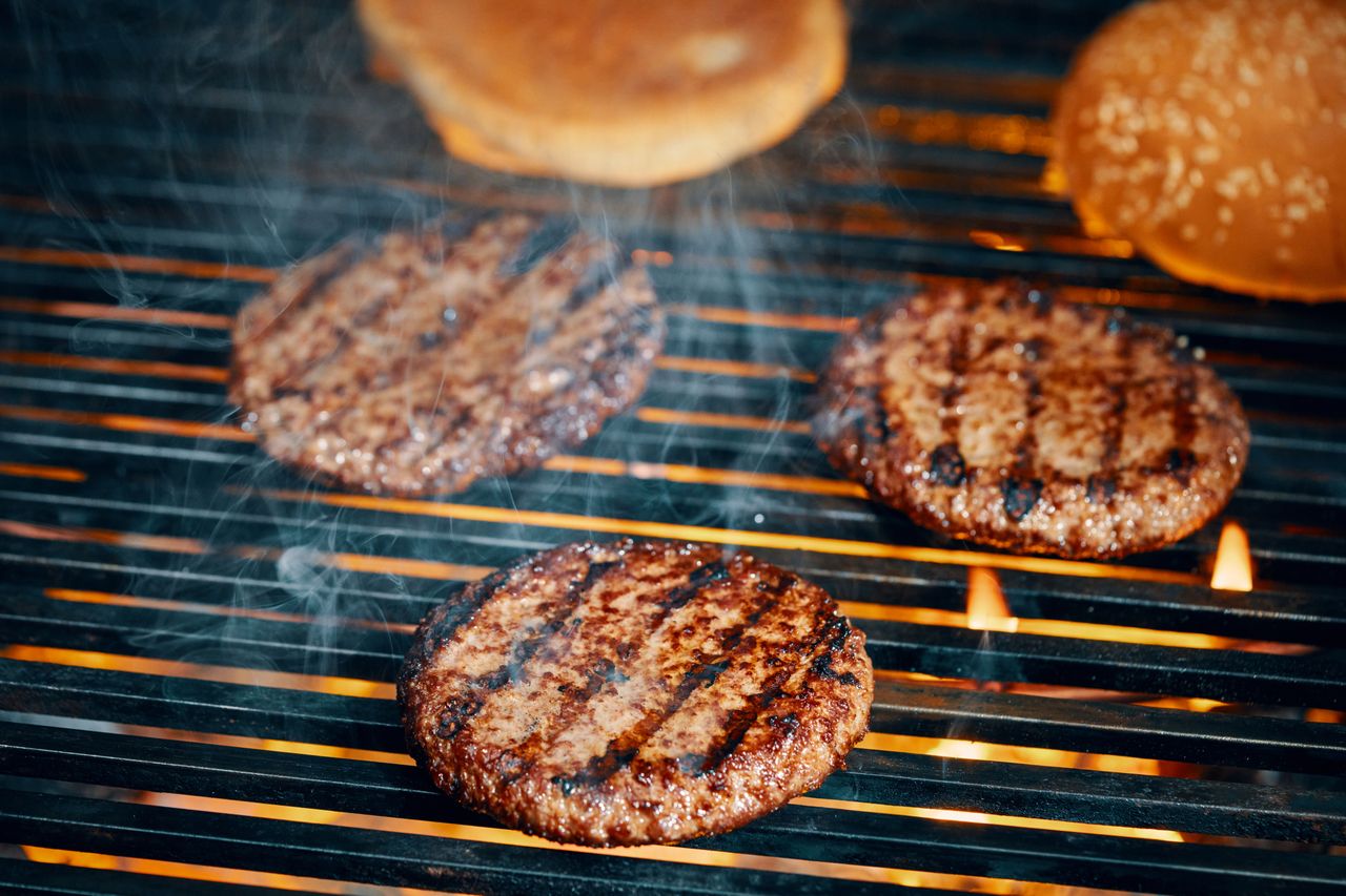 Grilled hamburger patties on a barbecue with buns in the background