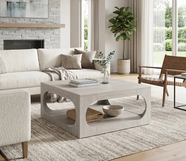 Modern living room with a minimalist, wooden coffee table, styled with decor items like a vase and book, next to a cream sofa and woven chair