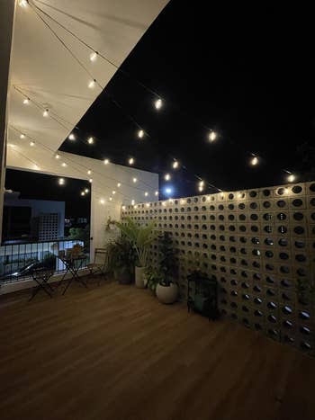 Outdoor patio with string lights, two chairs, a small table, and potted plants, creating a cozy ambiance for nighttime relaxation