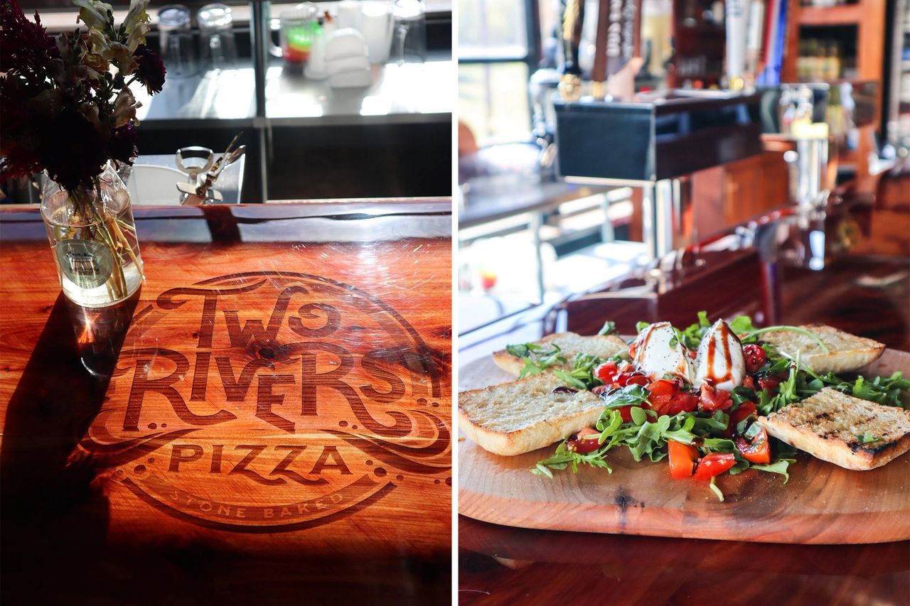 Two Rivers Pizza logo on a wooden counter plate with arugula salad and bread slices next to it
