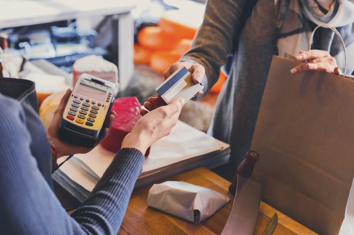 A person hands over their credit card at a grocery checkout register.