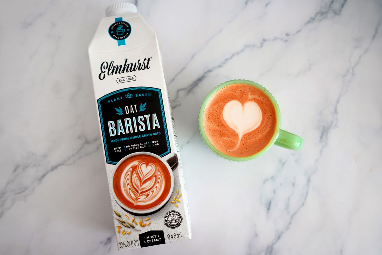 Carton of Elmhurst Oat Barista next to a cup of latte with heartshaped latte art