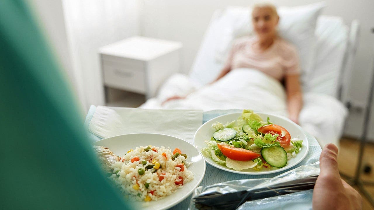 A nurse serves a patient a tray of food in a hospital.