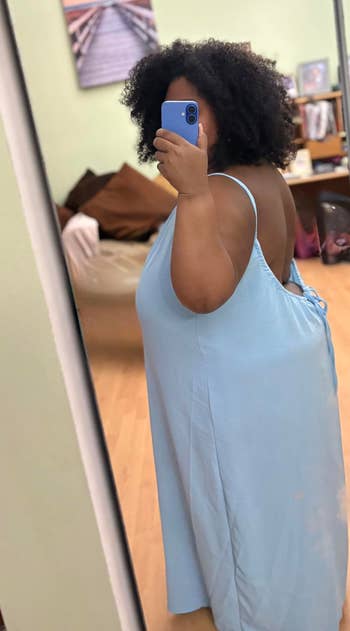 Person wearing a backless dress taking a mirror selfie in a room with a couch and beach photograph