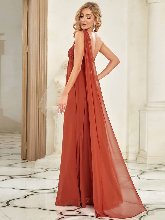Person in an elegant, flowing evening gown with a sheer cape, standing in a stylish, luxurious setting