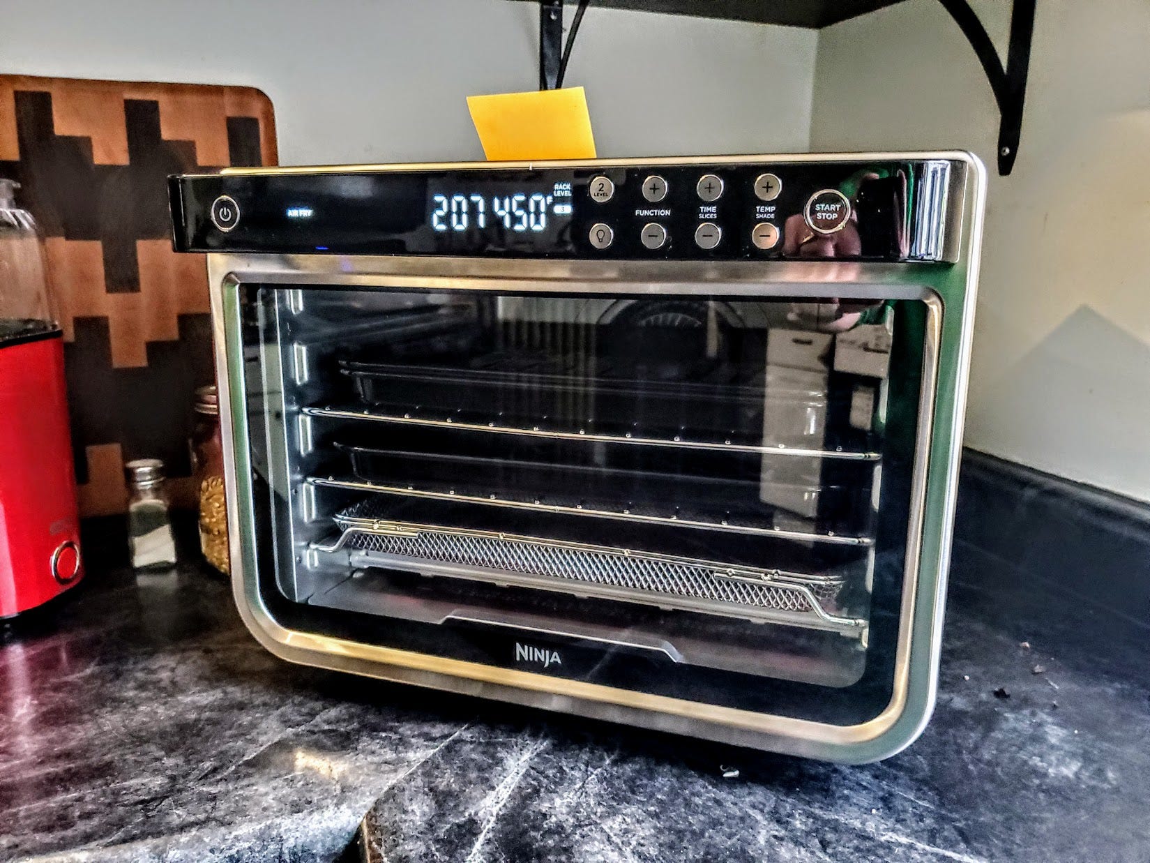 The Ninja Foodi XL Pro Air Fry Oven is displayed on a kitchen counter with all of its accessories inside.