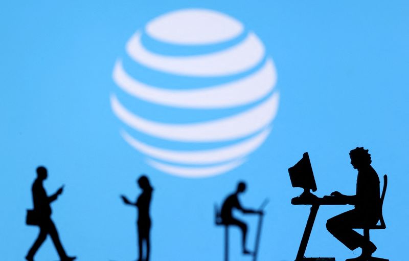 FILE PHOTO: Illustration shows small toy figures with laptops and smartphones in front of displayed AT&T logo