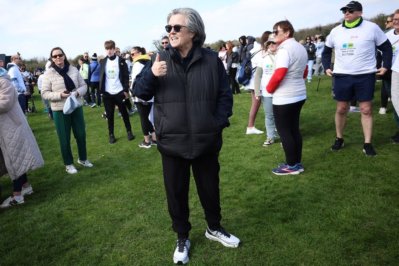 Rosie ODonnell standing outdoors on a grassy field surrounded by a group of people