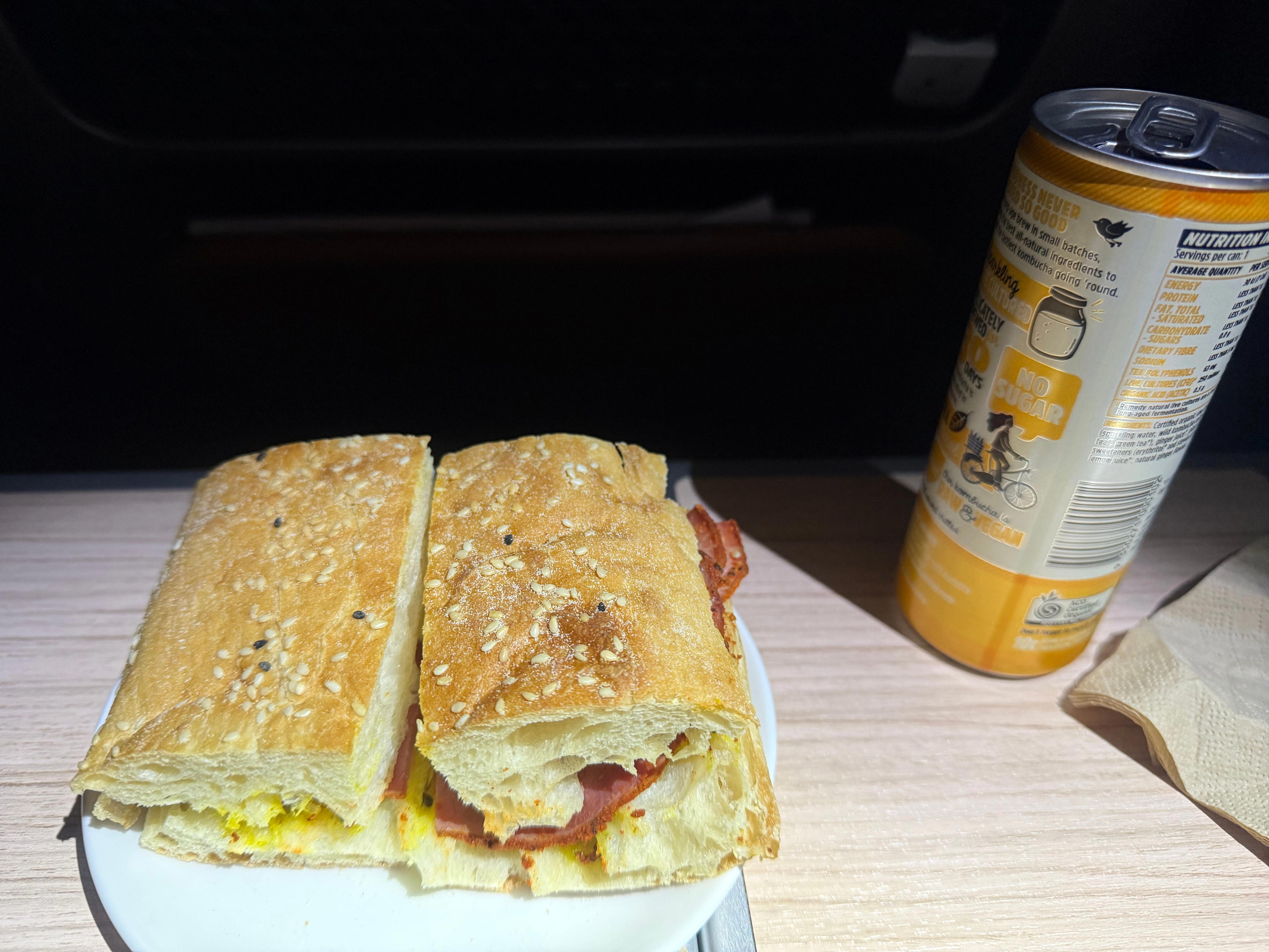 Pastrami and cheese sandwich and canned drink on tray table on Qantas premium flight