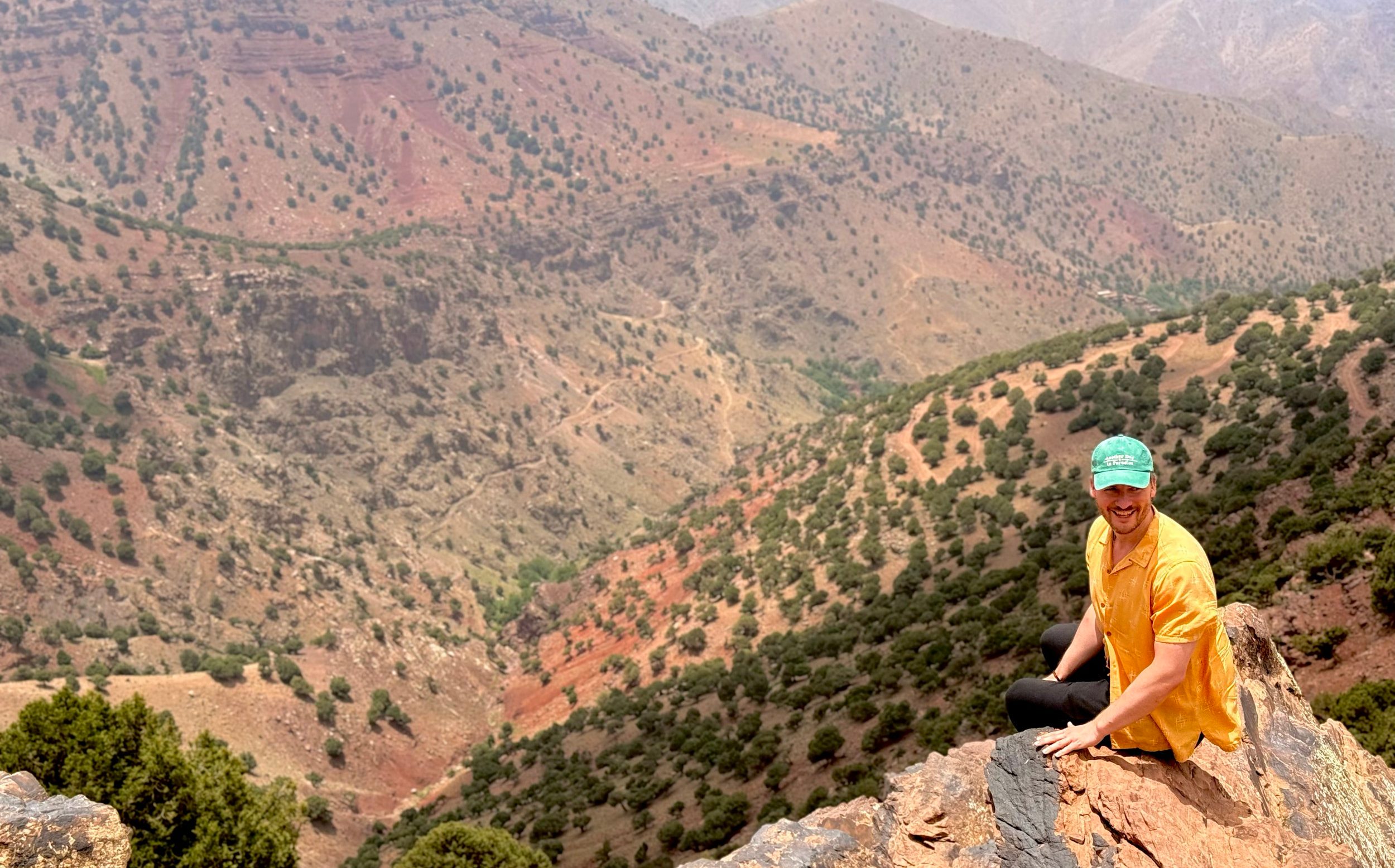 Matt Charlton smiles as he sits on a cliff edge overlooking a view of the Atlas Mountains in Morocco