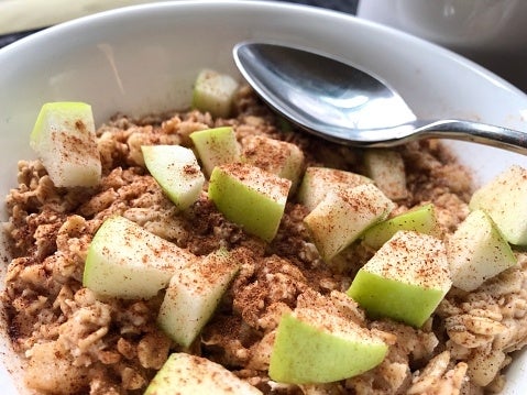 Bowl of oatmeal topped with diced green apples and cinnamon, with a spoon on the side