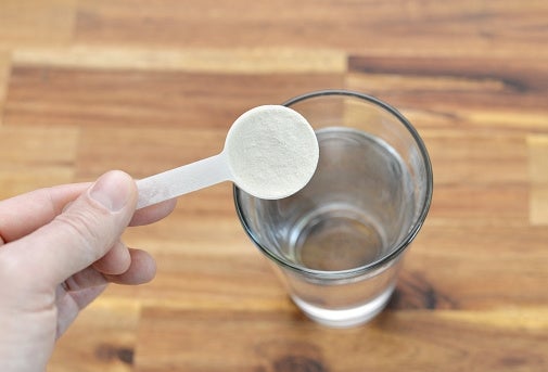 Scoop of white powder held over an empty glass, suggesting a dietary supplement or health-related use