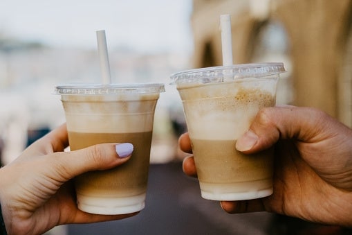 Two people holding plastic cups with iced coffee, each with a straw, in an outdoor setting