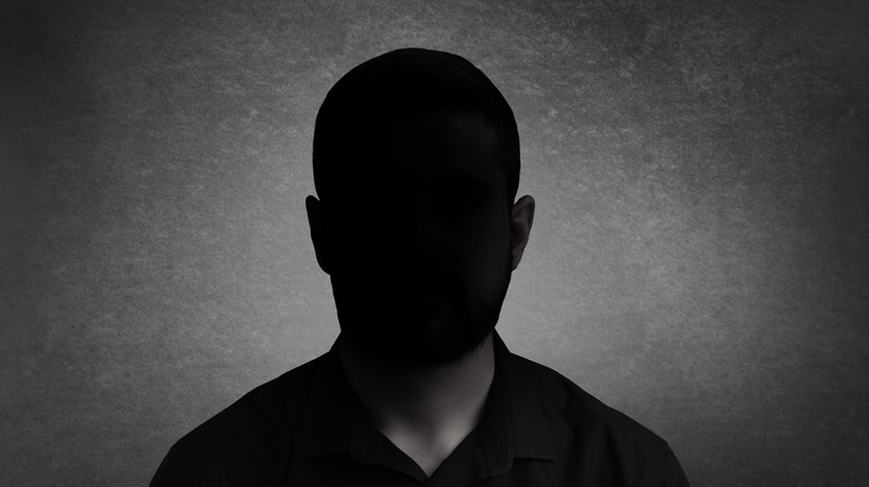 A person in front of a gray background with their face obscured by darkness