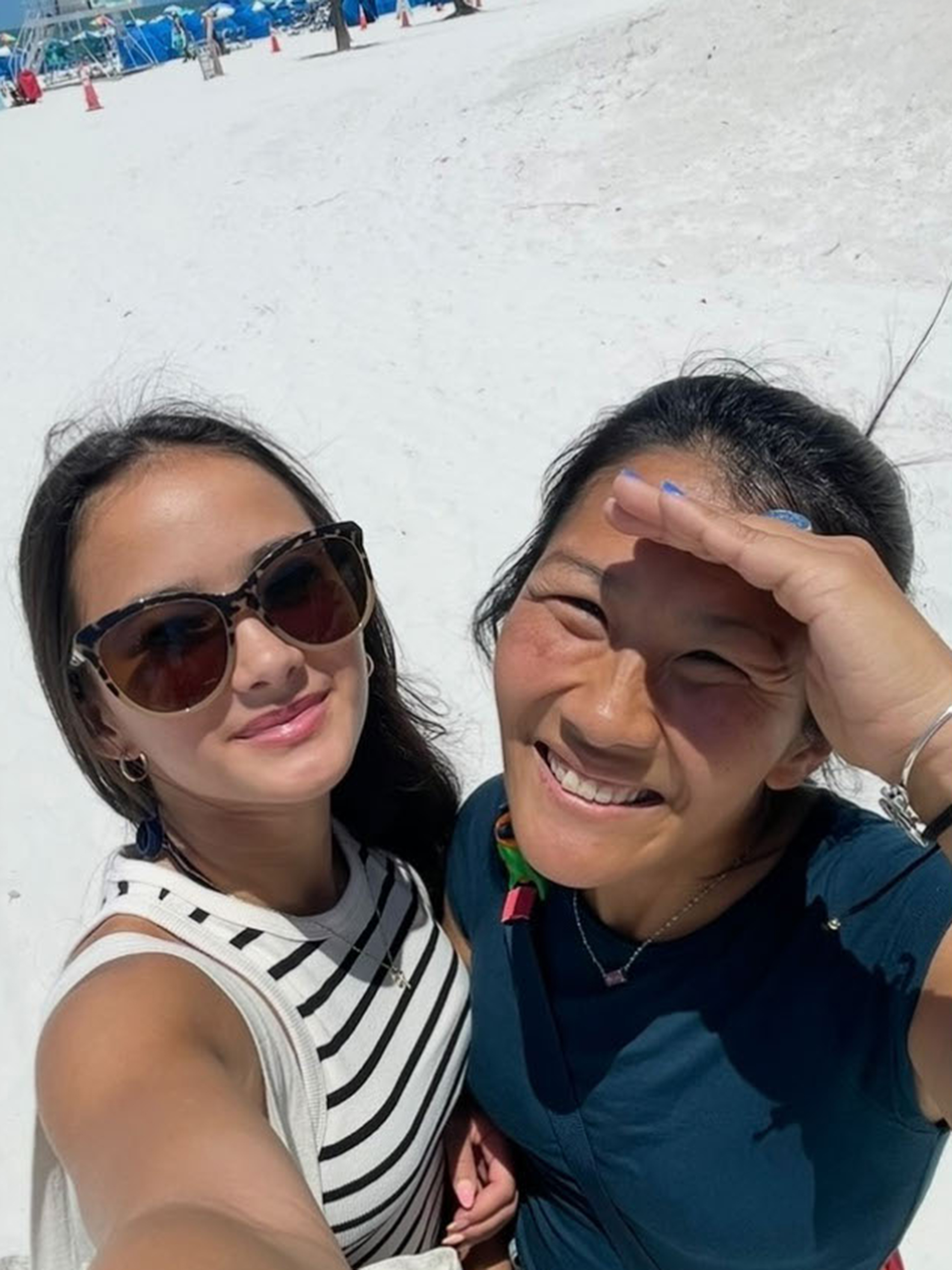 Two women, Kaylee Hottle and Ketsi Carlson, smile for a selfie on a beach.