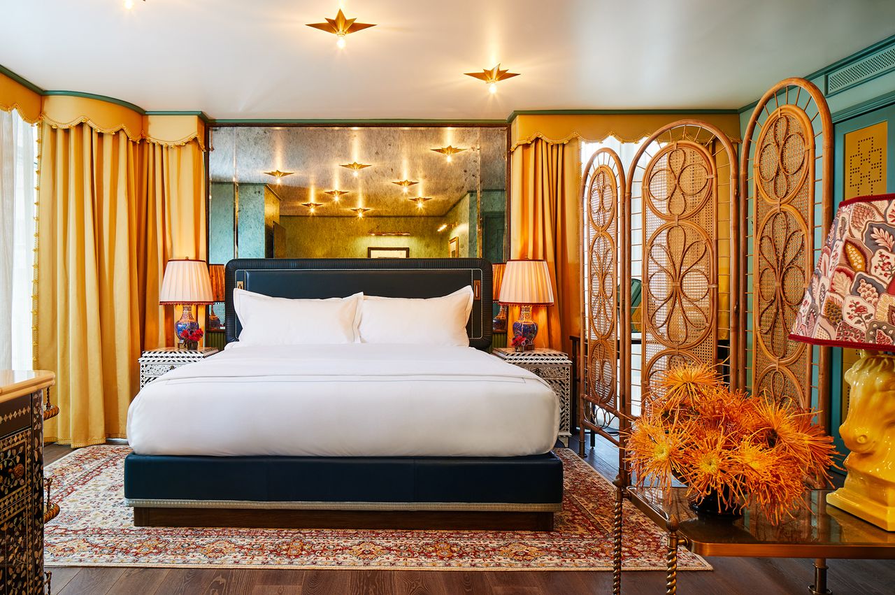 A welldesigned hotel suite featuring a large bed with white linens decorative lighting fixtures curtains and unique furnishings