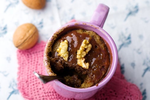 Mug cake topped with walnuts and chocolate, served in a pink mug on a knitted cloth, with whole walnuts nearby