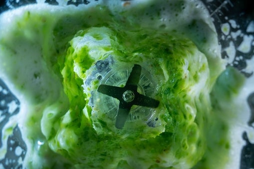 Top view of a blender mixing green ingredients, creating a frothy texture around the blades