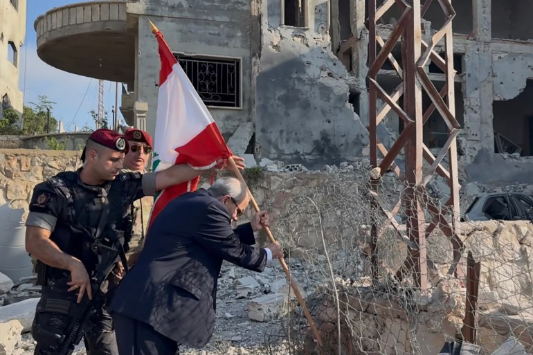 This handout picture released by the Lebanese prime minister's media office shows Lebanese Prime Minister Nawaf Salam placing a national flag along a damaged street in the southern village of Zawtar al-Gharbiya on July 22, 2026, after the withdrawal of Israeli troops from the area. Beirut is working towards a