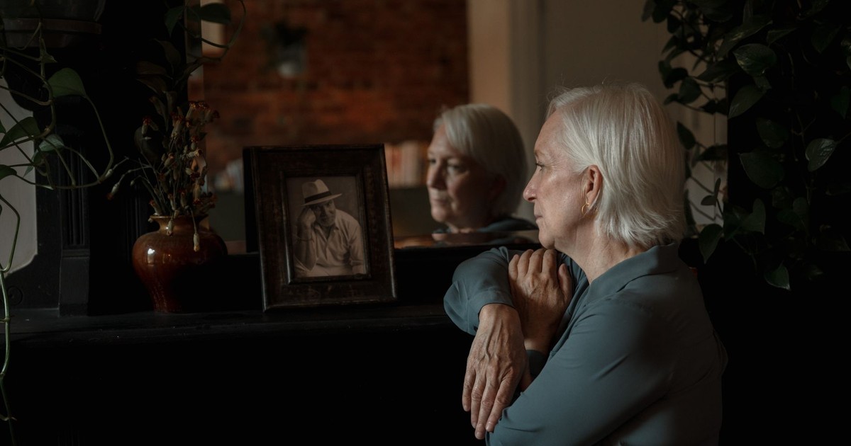 Elderly woman reminisces while looking at an old photograph indoors.