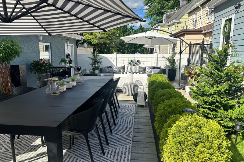 Black table and chairs under black and white striped umbrella in backyard.