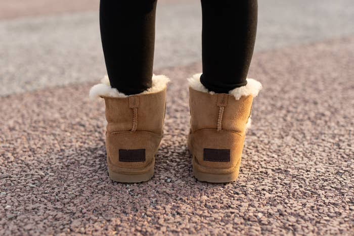 Person wearing fluffy winter boots and black leggings standing on a textured ground
