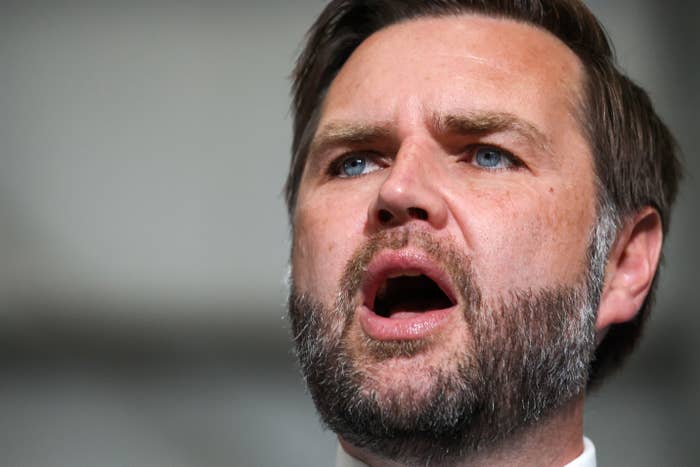 A person with a beard is speaking with their mouth open, appearing to deliver an emphatic speech or announcement